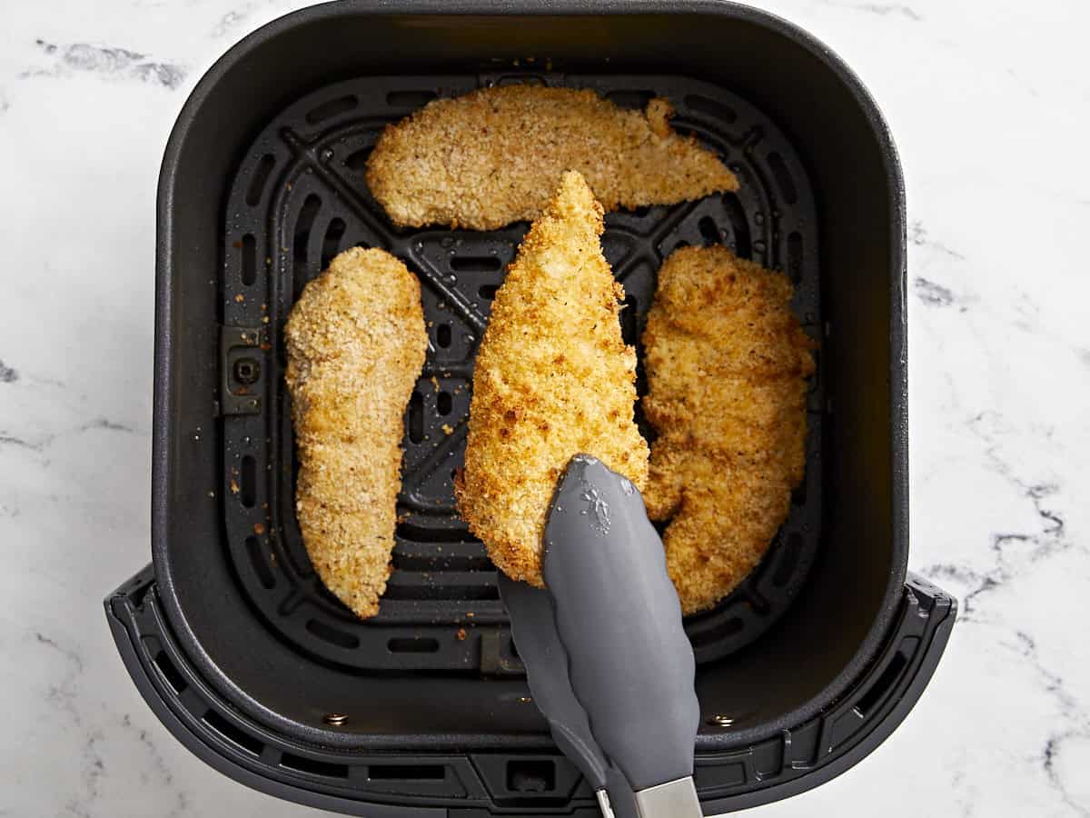 Overhead view of chicken tenders being flipped in air fryer basket.