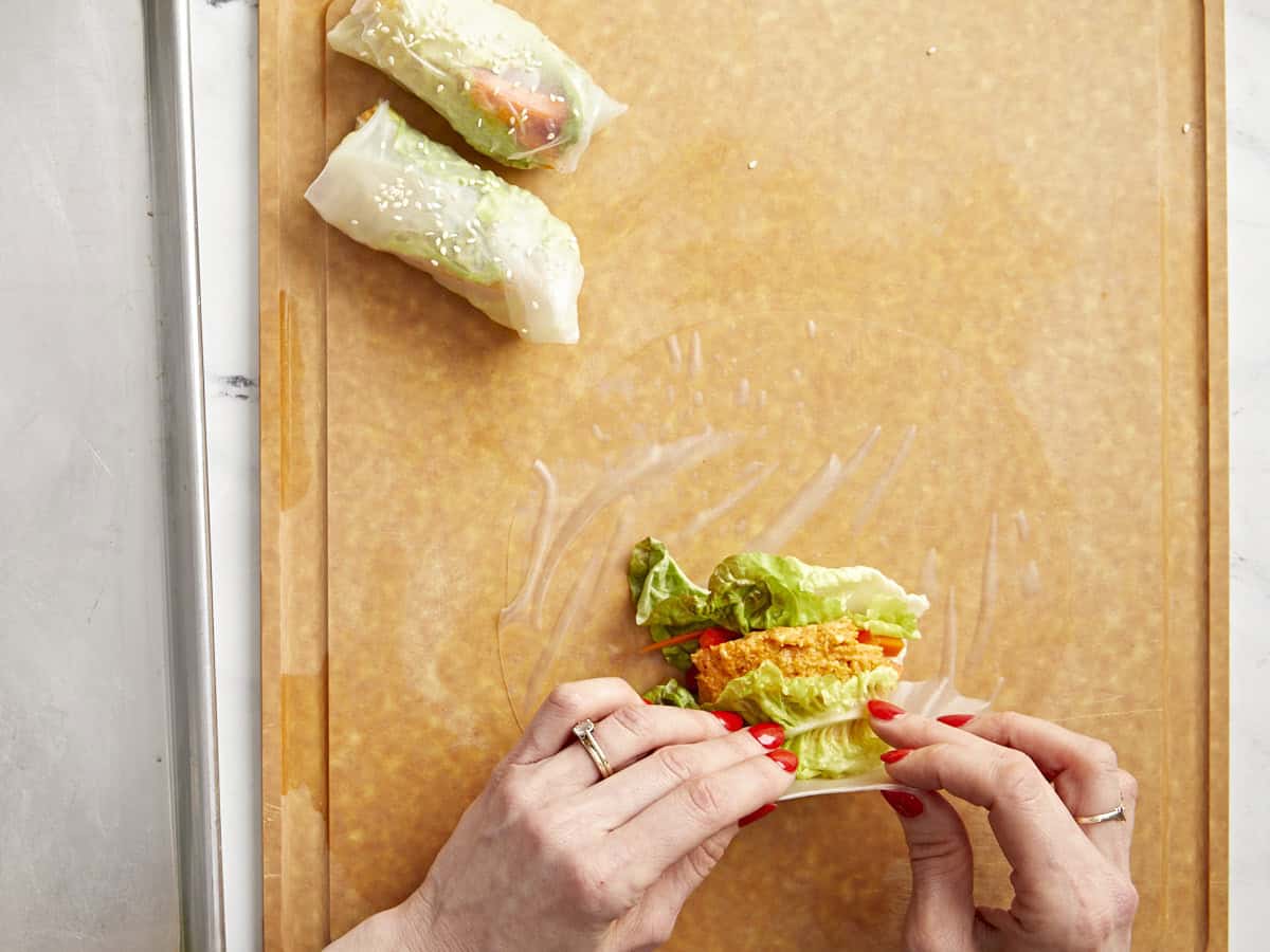 filling a rice paper wrapper with kimchi and veggies.