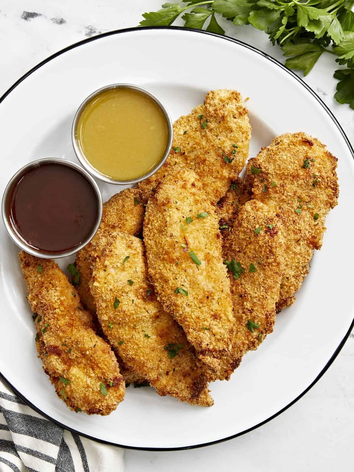 Overhead view of Air Fryer Chicken Tenders on a white serving plate with two dipping sauces on the side.