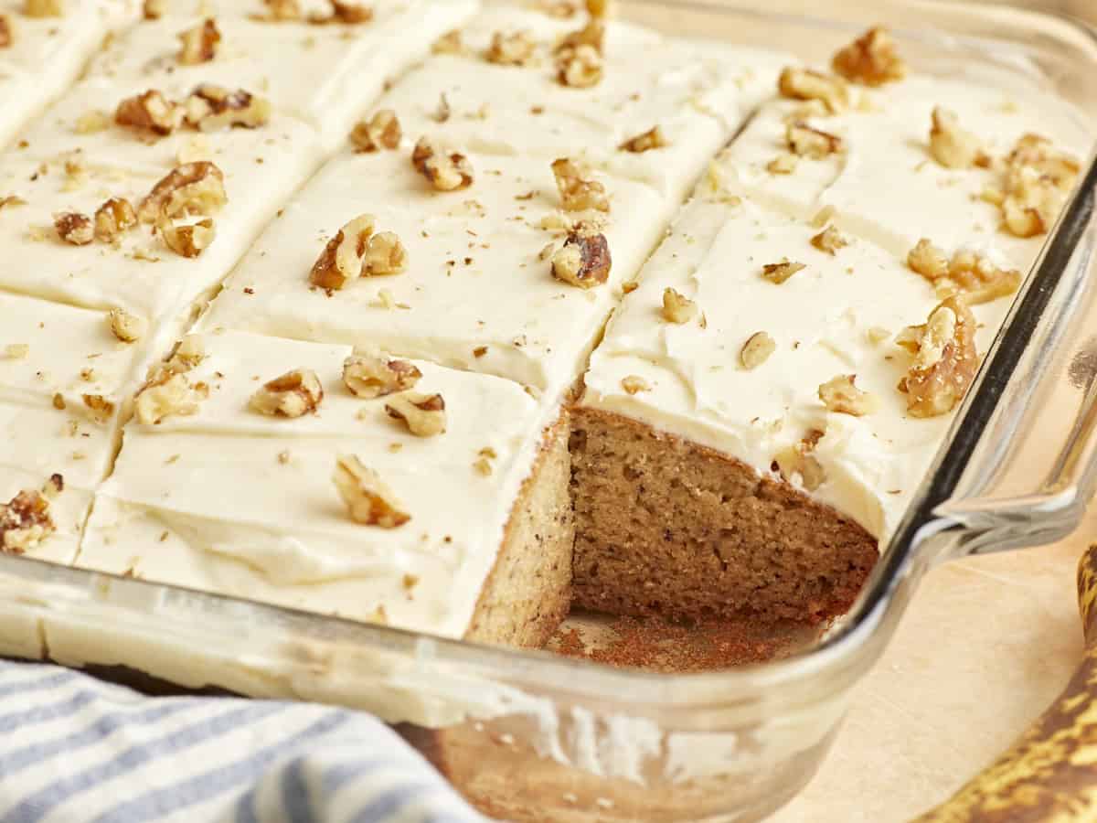 three-quarters view of a cut banana cake in a glass baking dish missing a slice.