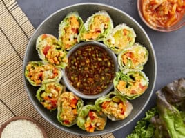 overhead view of kimchi spring rolls on a platter with a bowl of sauce in the middle.