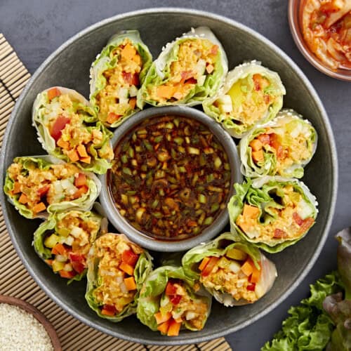 overhead view of kimchi spring rolls on a platter with a bowl of sauce in the middle.