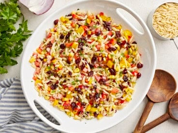 Overhead view of Orzo Pasta Salad in a white serving bowl with wood serving spoons on the side.