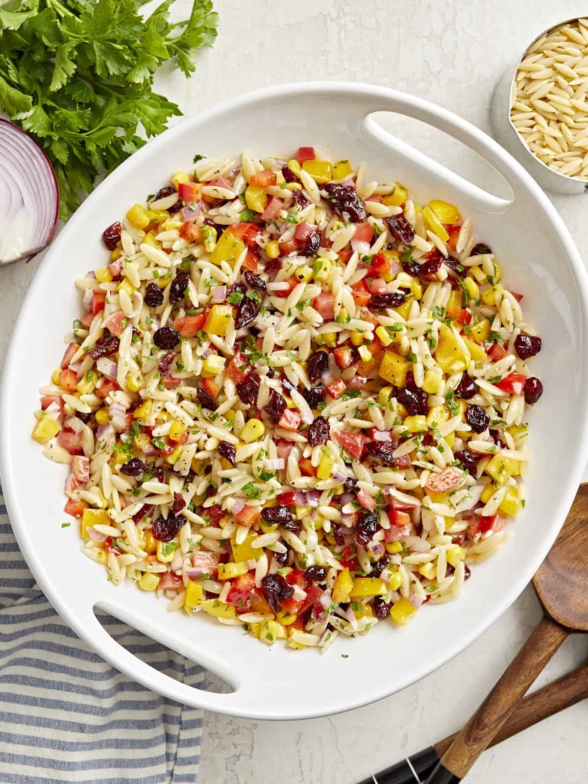 Overhead view of Orzo Pasta Salad in a white serving bowl with wood serving spoons on the side.