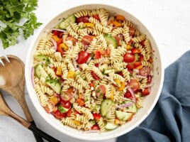 Overhead view of pasta salad in a large white serving bowl with wood serving utensils on the side.