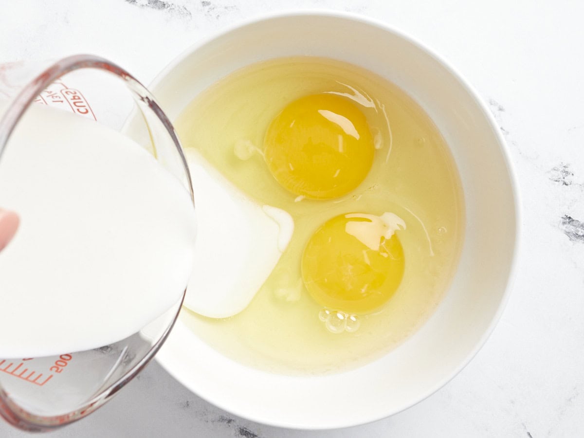 pouring buttermilk into a bowl of eggs.