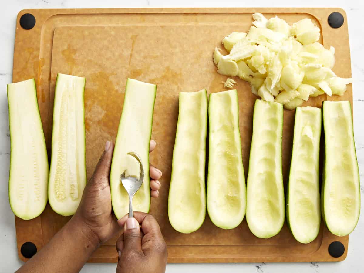 The flesh being scooped out of Zucchini on a cutting board.