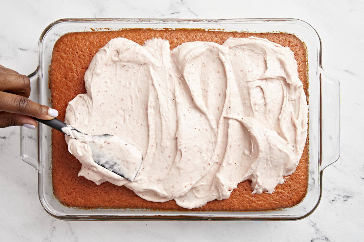 Strawberry frosting being spread on to strawberry cake.