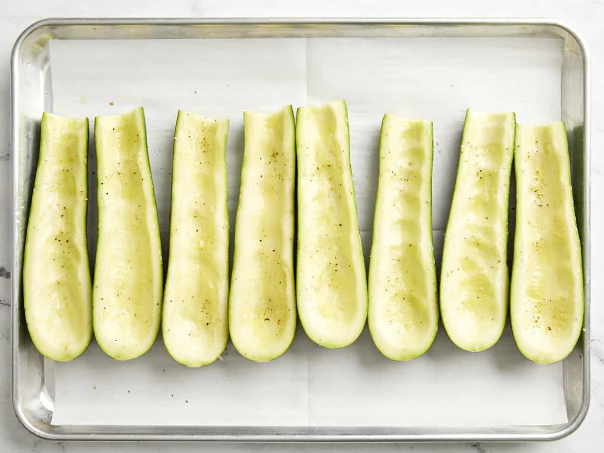 Zucchini scooped out, cut in half, and seasoned on a parchment lined baking sheet. 