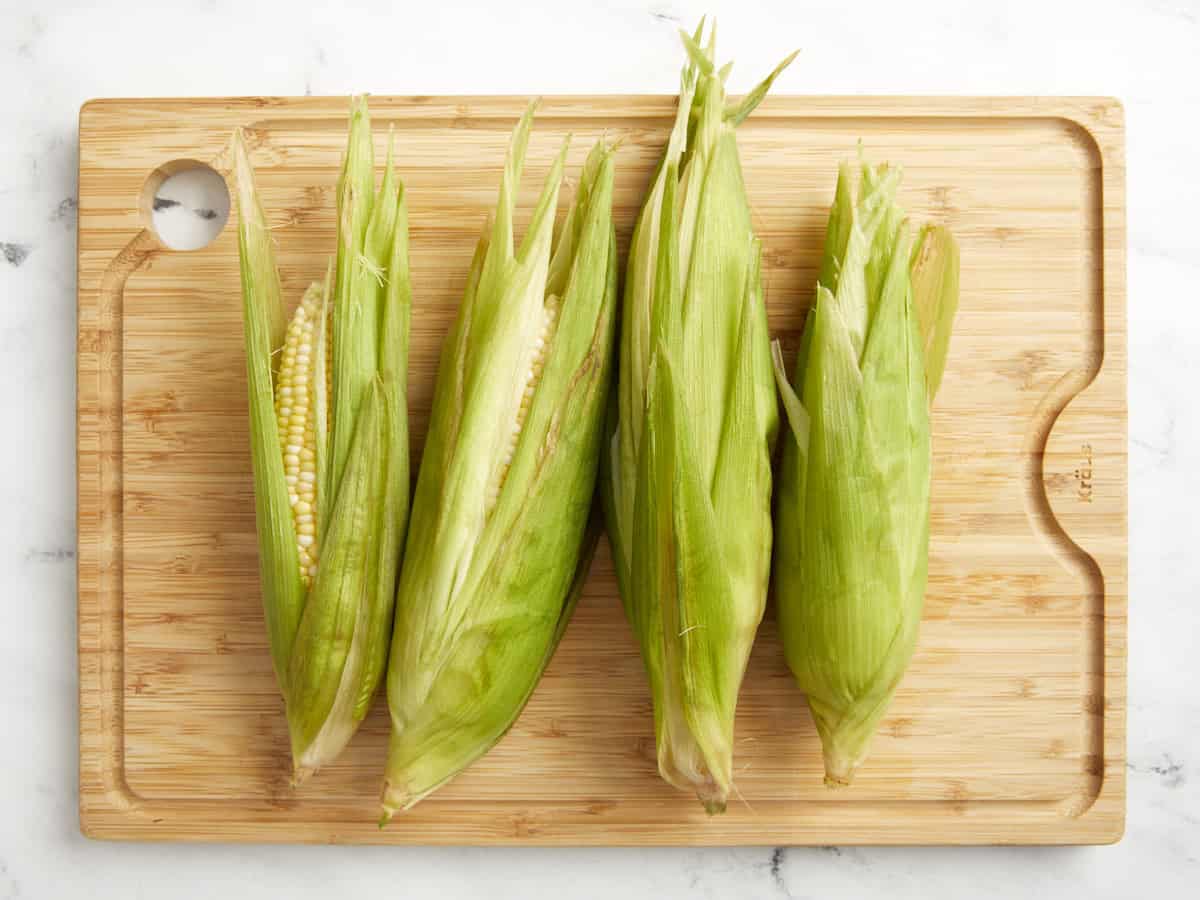 4 peeled ears of corn with the husks pulled back over the cobs.