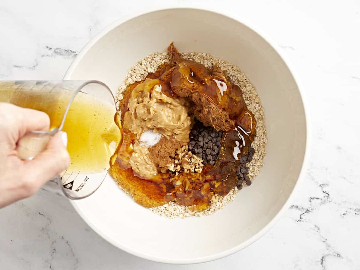 pouring honey into a bowl with granola bar ingredients.