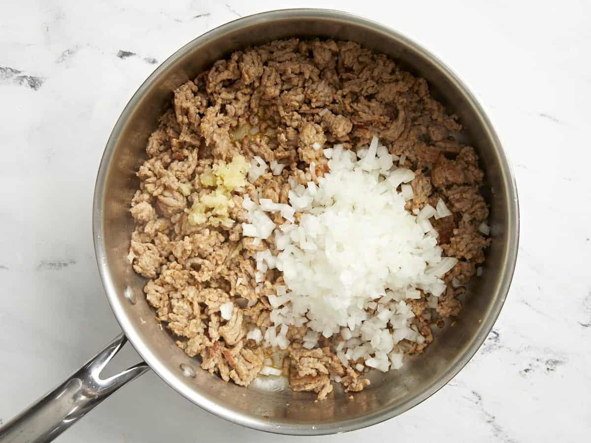 Browned Italian sausage, diced onion, and minced garlic in a pan.