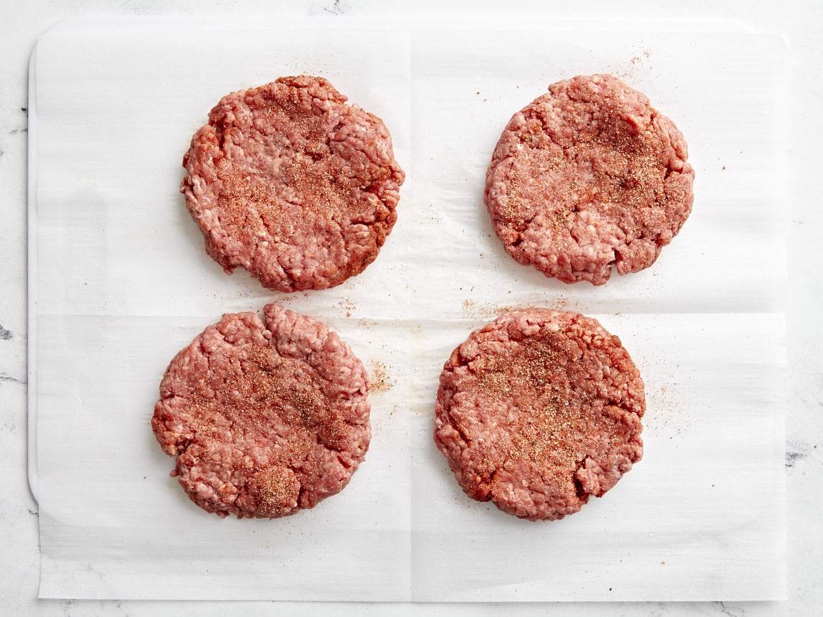 Four ground beef hamburger patties with hamburger seasoning on top.