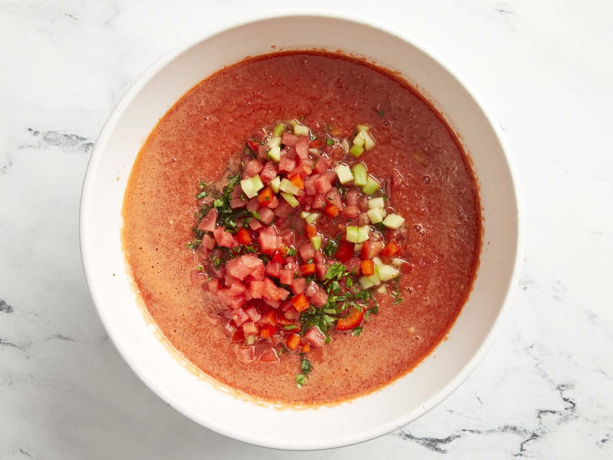 a bowl of watermelon gazpacho topped with diced fruits and vegetables.