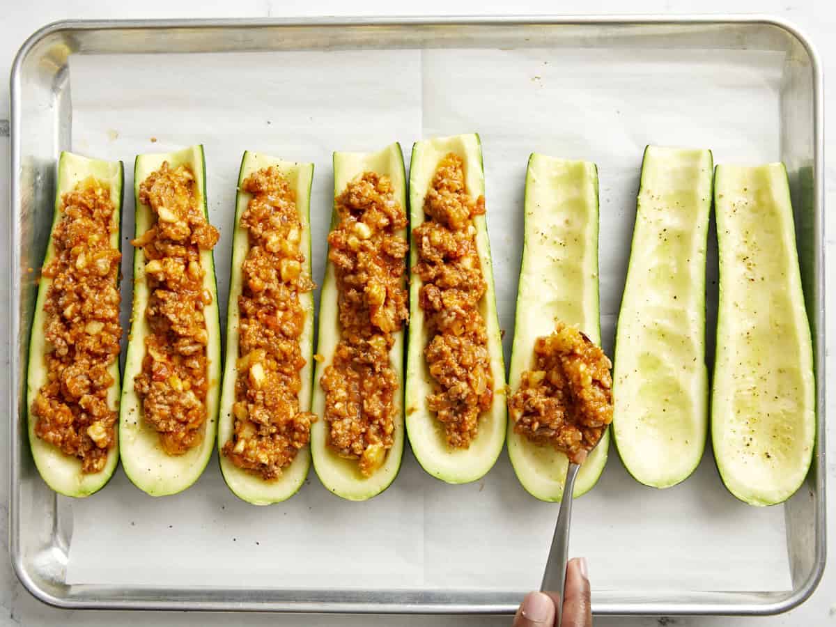 Adding the sausage mixture to the inside of the zucchini boats. 