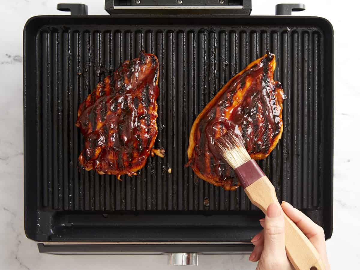 basting grilled chicken breasts with bbq sauce on an indoor grill.