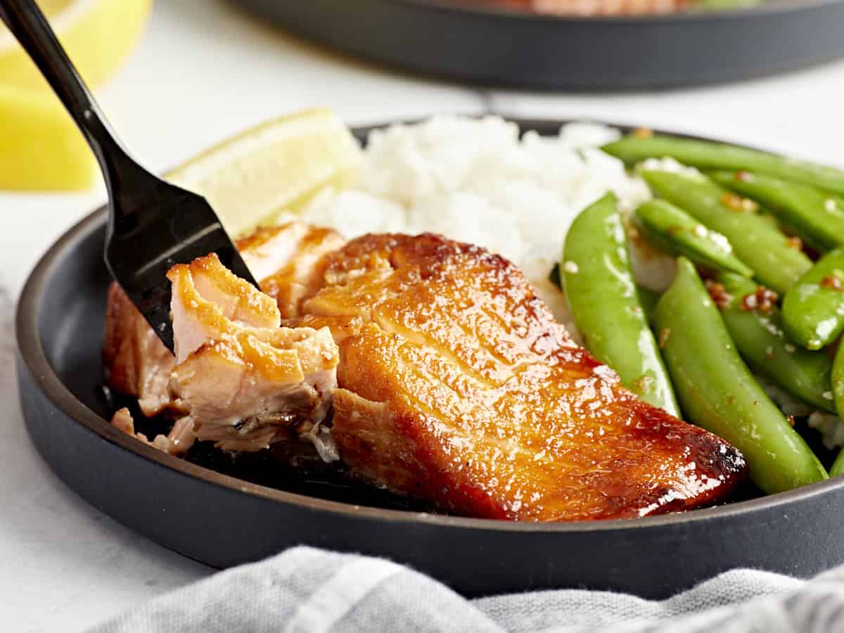 a forkful of air fryer salmon in front of a serving on a plate with rice and peas.