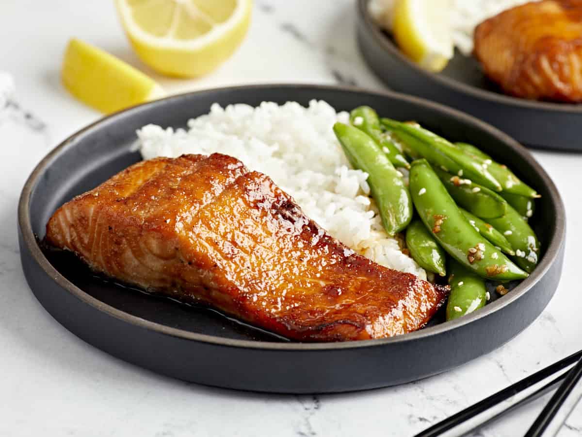 side view of a serving of air fryer salmon on a black plate with rice and peas.