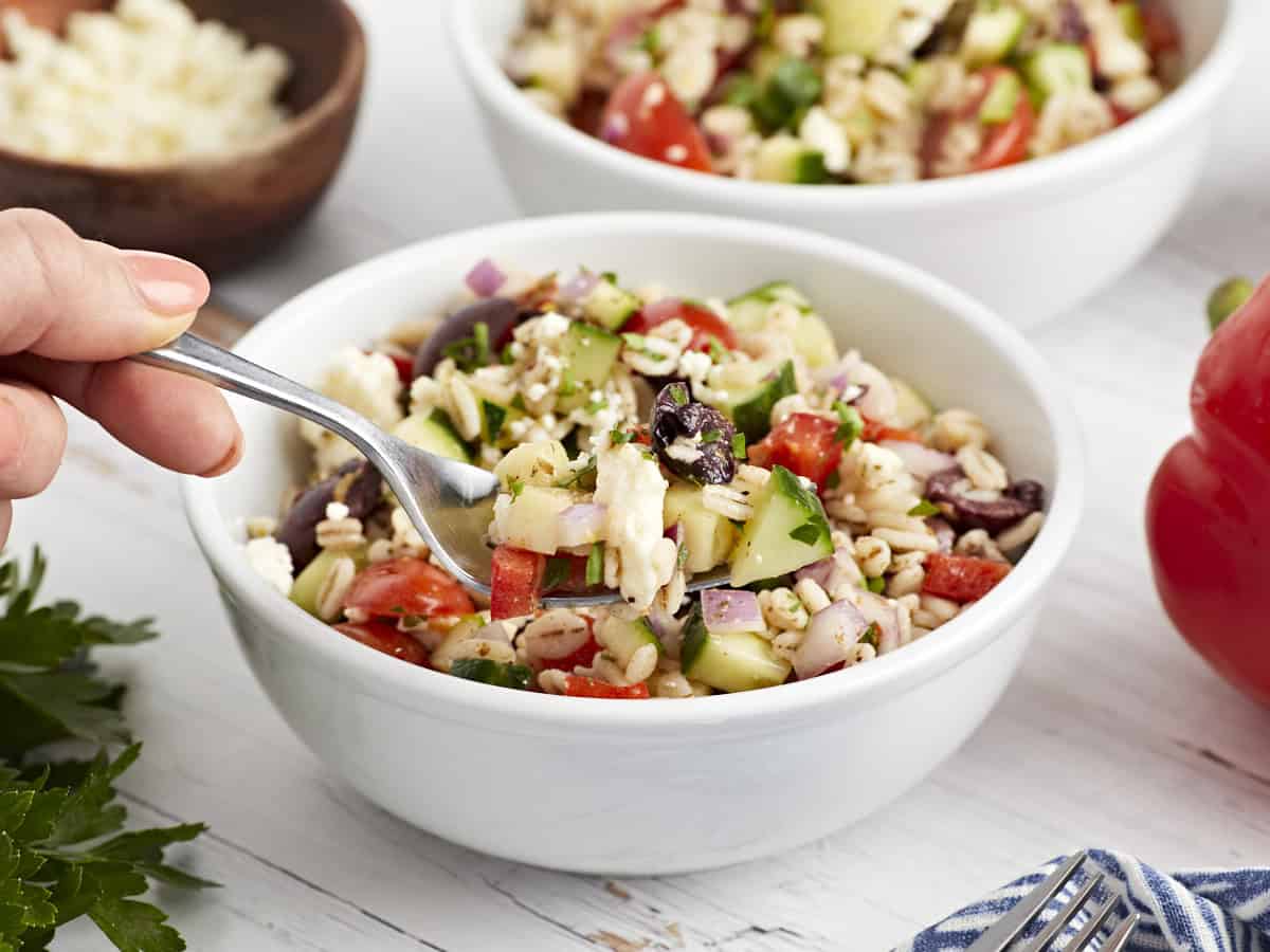 holding a forkful of barley salad over a serving in a bowl.