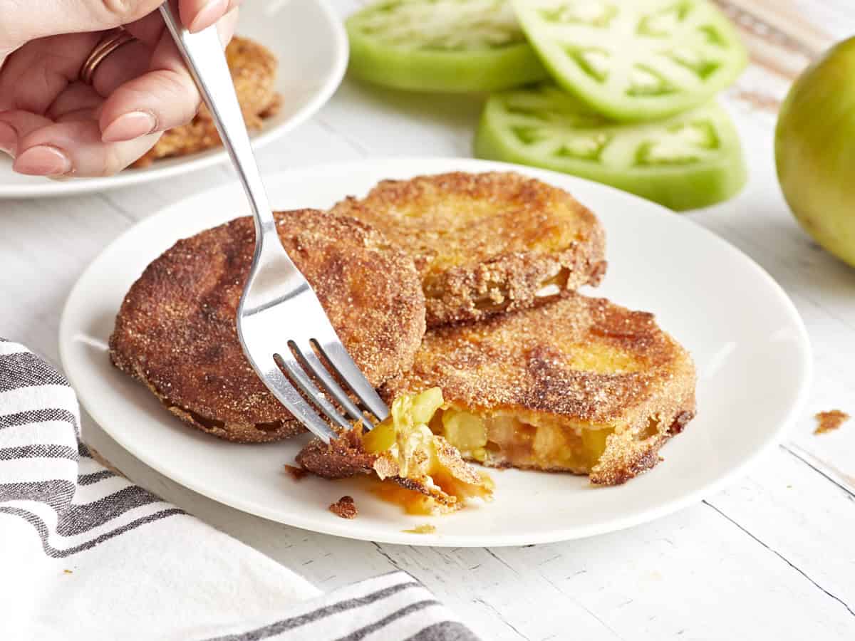 a fork stabbing a piece of cut fried green tomato on a white plate.