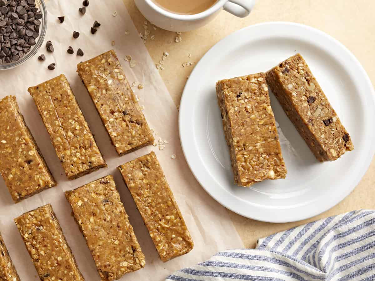 overhead view of 2 granola bars on a white plate next to granola bars on parchment.