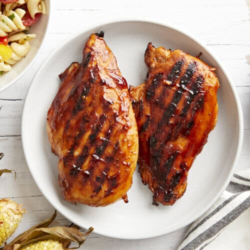 overhead view of 2 grilled bbq chicken breasts on a white plate.