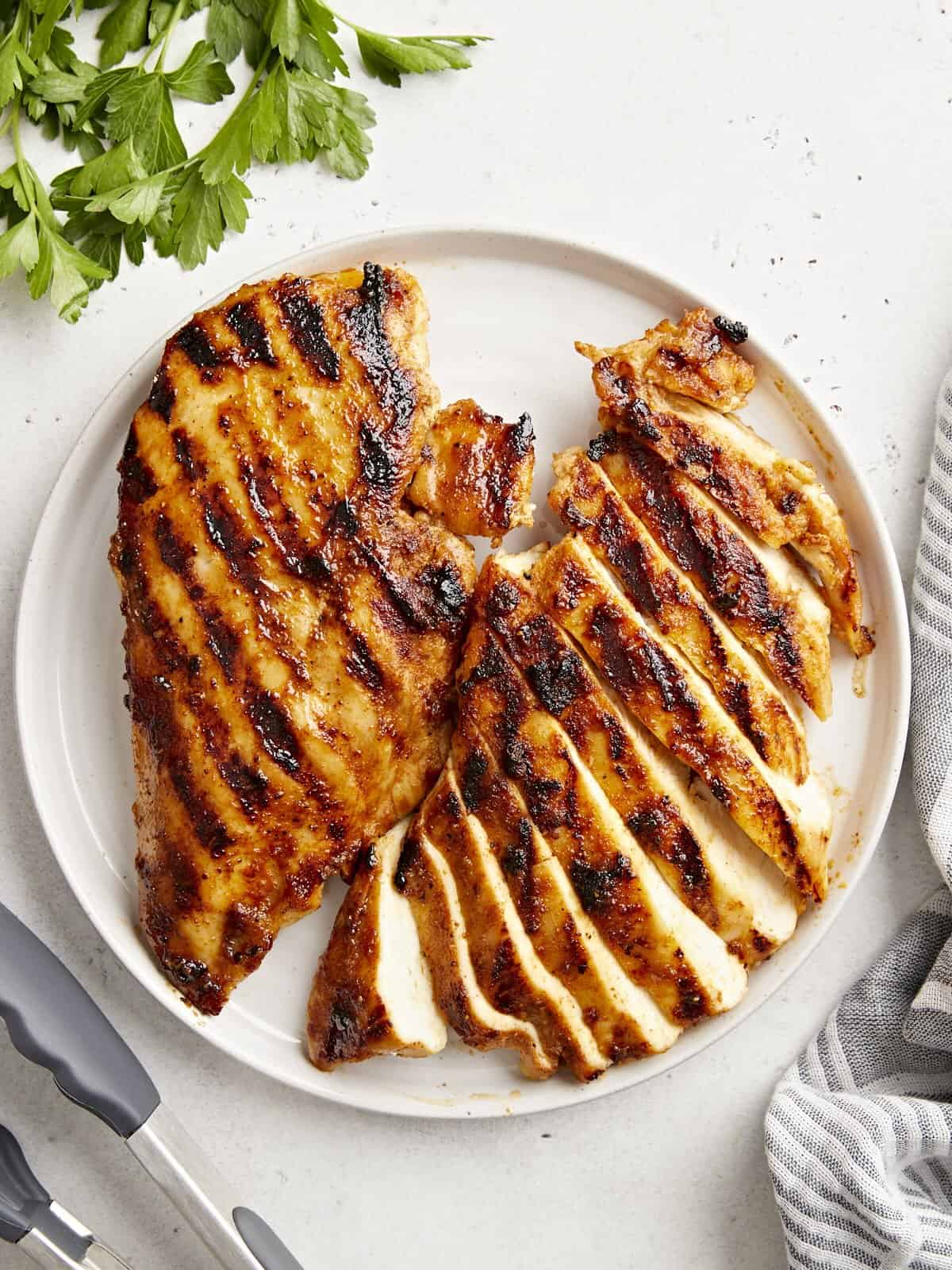 overhead view of 2 sliced grilled chicken breasts on a white plate.