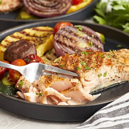 cutting a piece of grilled salmon on a black plate with a fork.