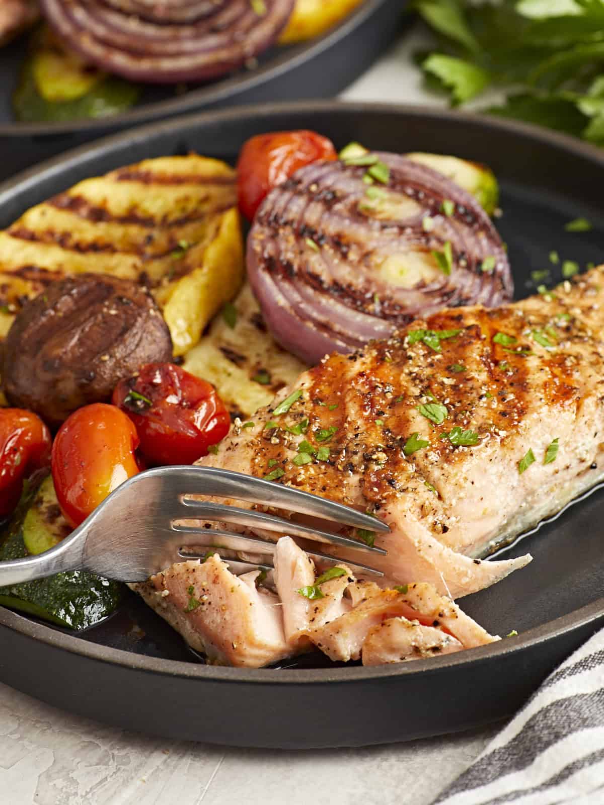 cutting a piece of grilled salmon on a black plate with a fork.