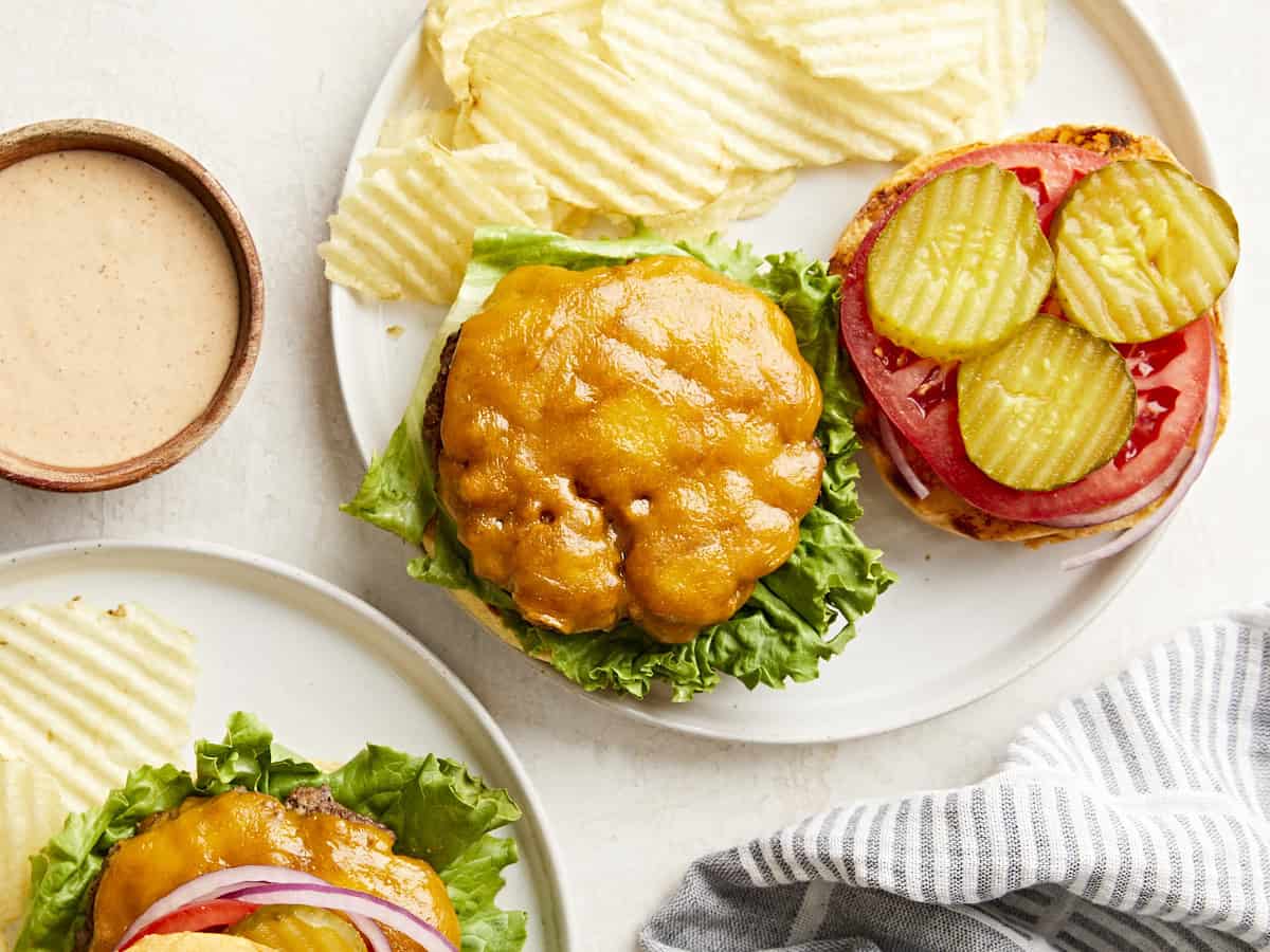 Overhead view of homemade hamburgers on a plate with toppings and chips on the side.