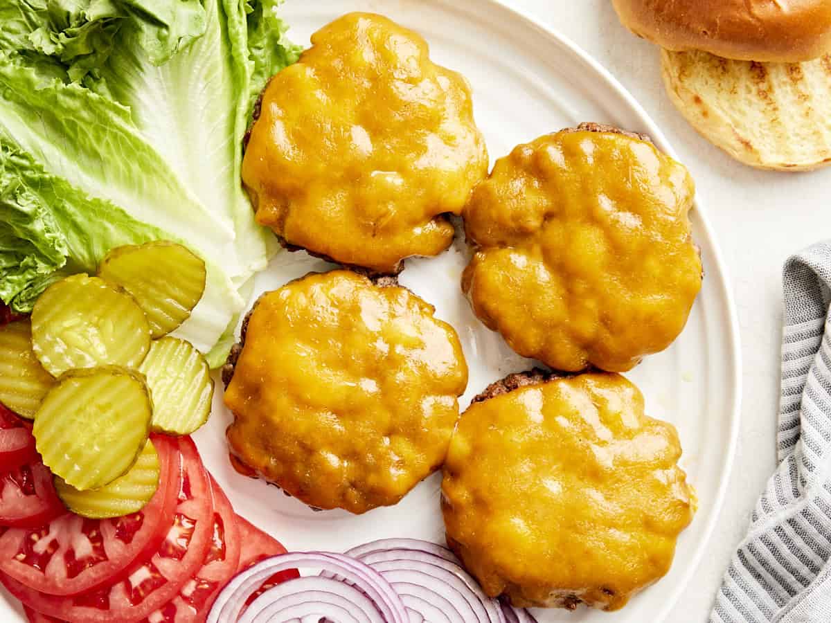 Overhead view of homemade hamburgers on a serving platter with toppings on the side.