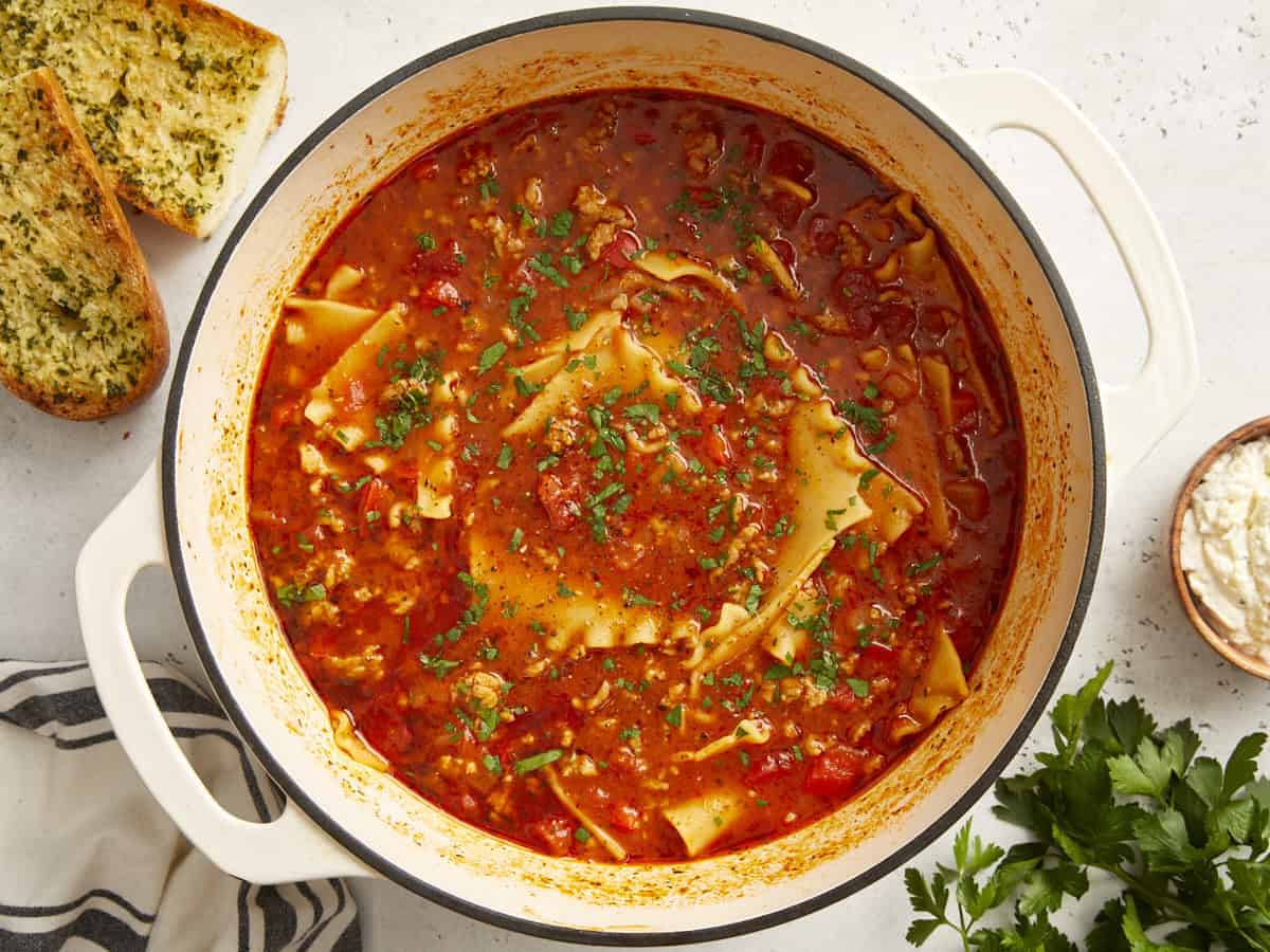 Overhead view of lasagna soup in a dutch oven with garlic bread on the side.