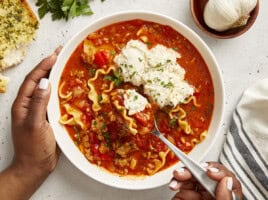 Overhead view of Lasagna Soup in a white bowl with a hand holding a spoon lifting some out.