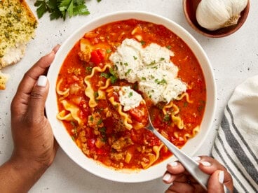 Overhead view of Lasagna Soup in a white bowl with a hand holding a spoon lifting some out.