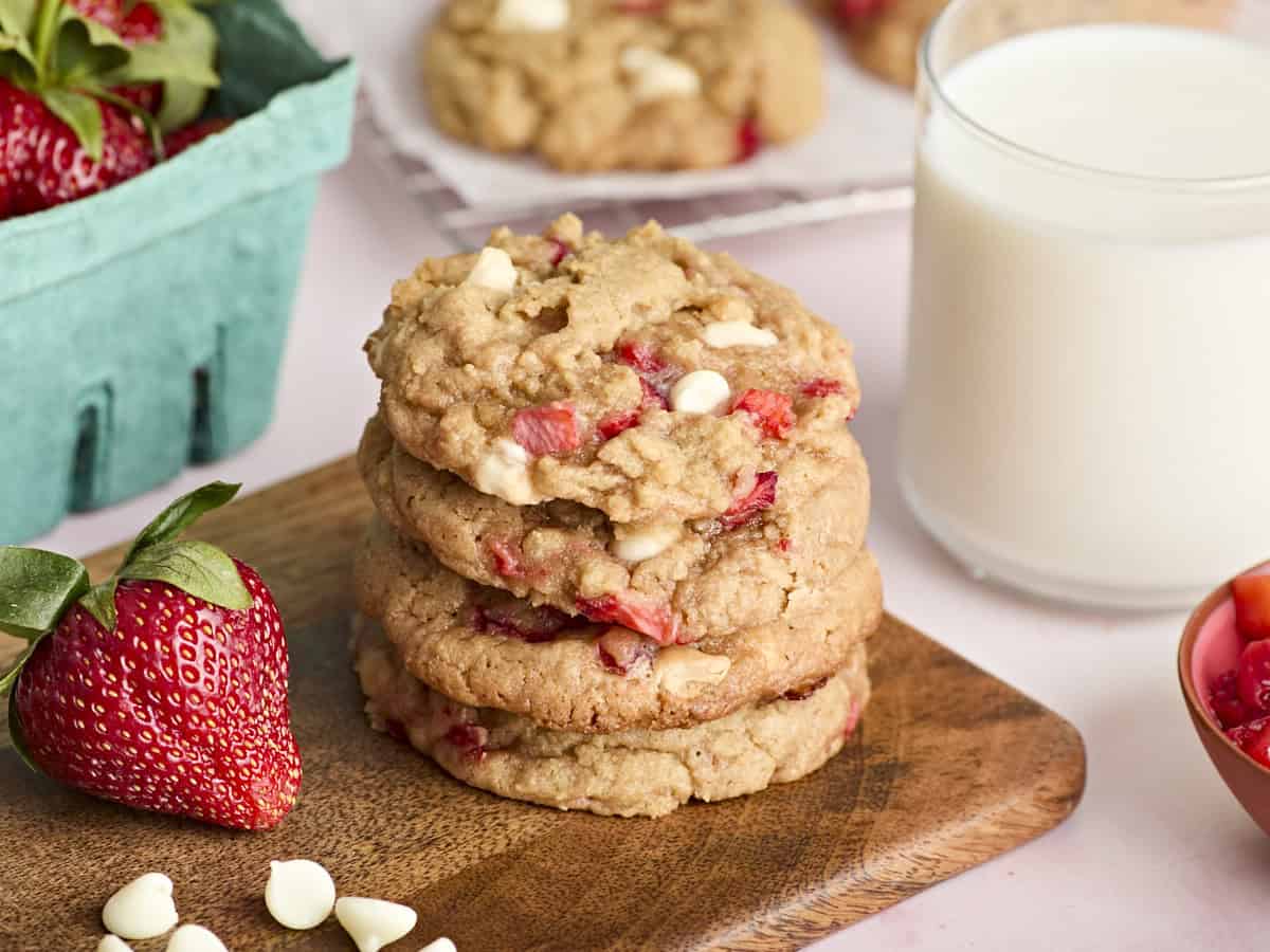 4 stacked strawberry cookies on a wood cutting board.