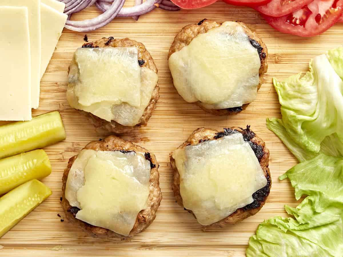 4 turkey burgers topped with melted cheese on a cutting board.