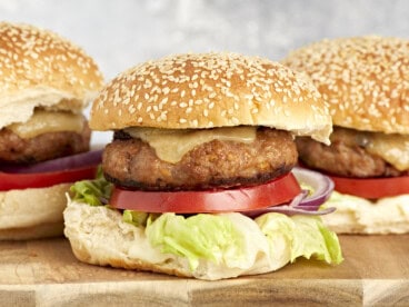 side view of turkey burgers topped with cheese, lettuce, and tomato on buns.