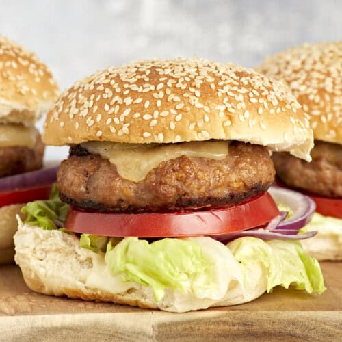 side view of turkey burgers topped with cheese, lettuce, and tomato on buns.