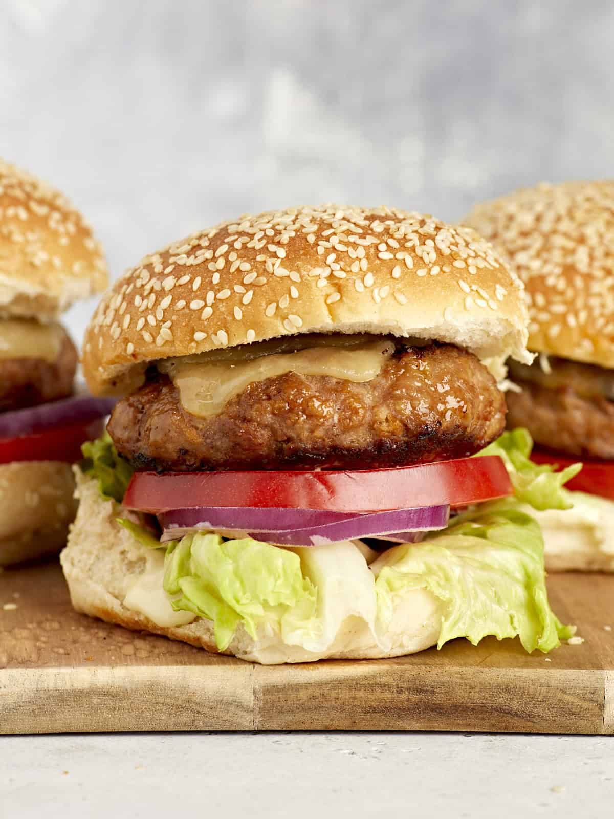 side view of turkey burgers topped with cheese, lettuce, and tomato on buns.