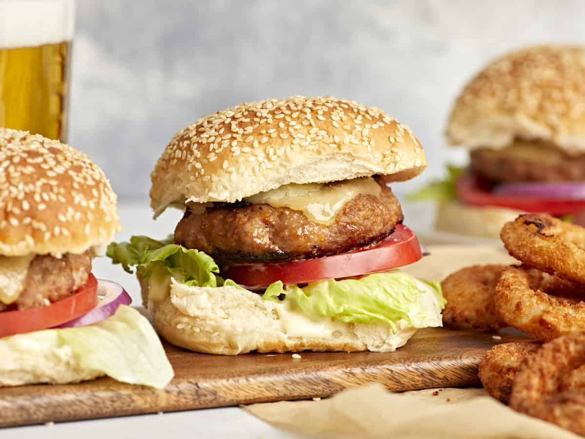 side view of turkey burgers topped with cheese, lettuce, and tomato on buns.