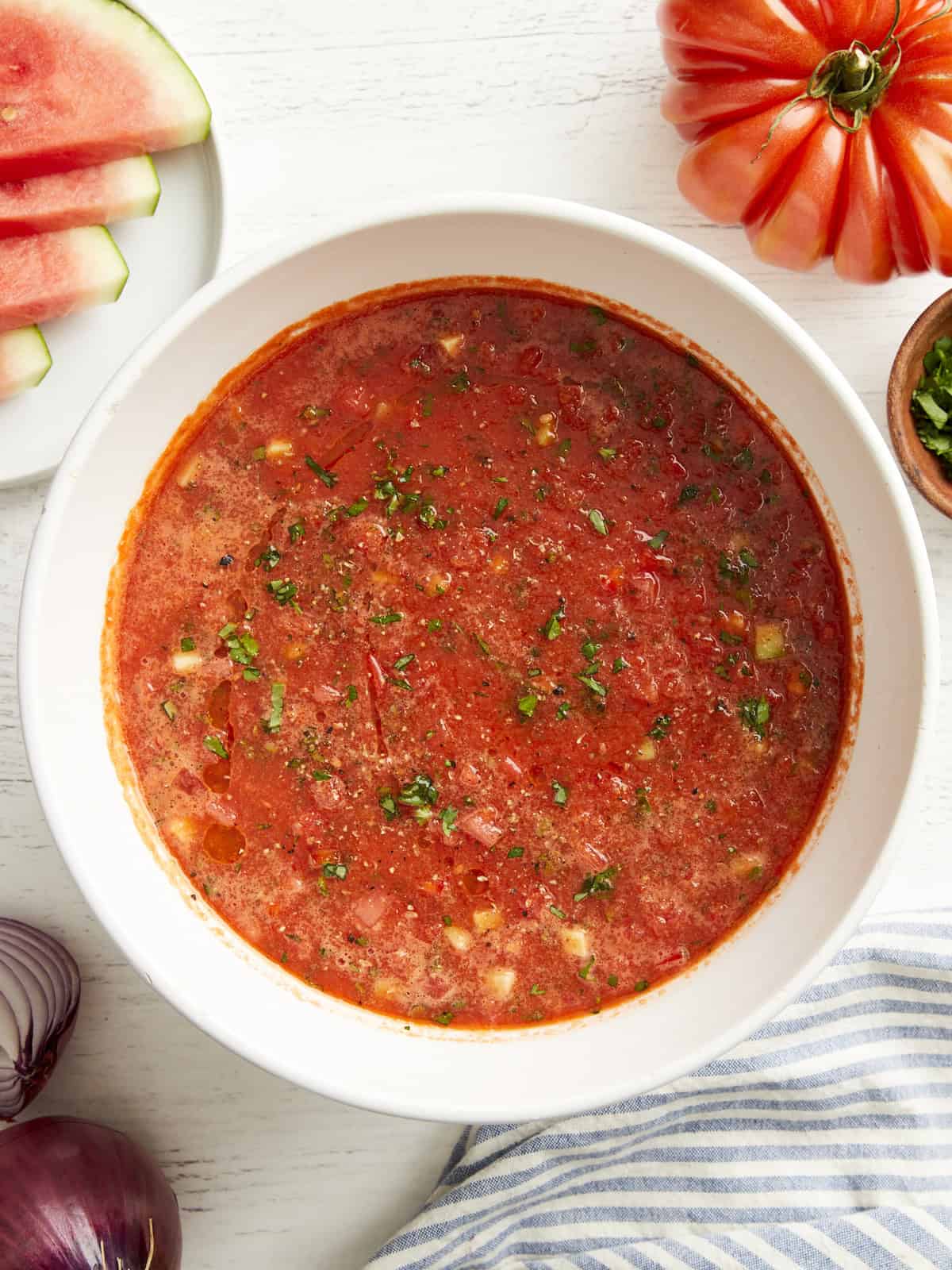 overhead view of watermelon gazpacho in a white bowl with minced fresh herbs.