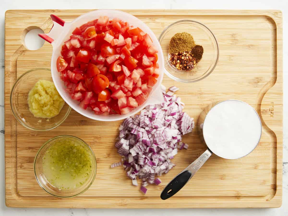 Ingredients for tomato relish on a wooden chopping board.