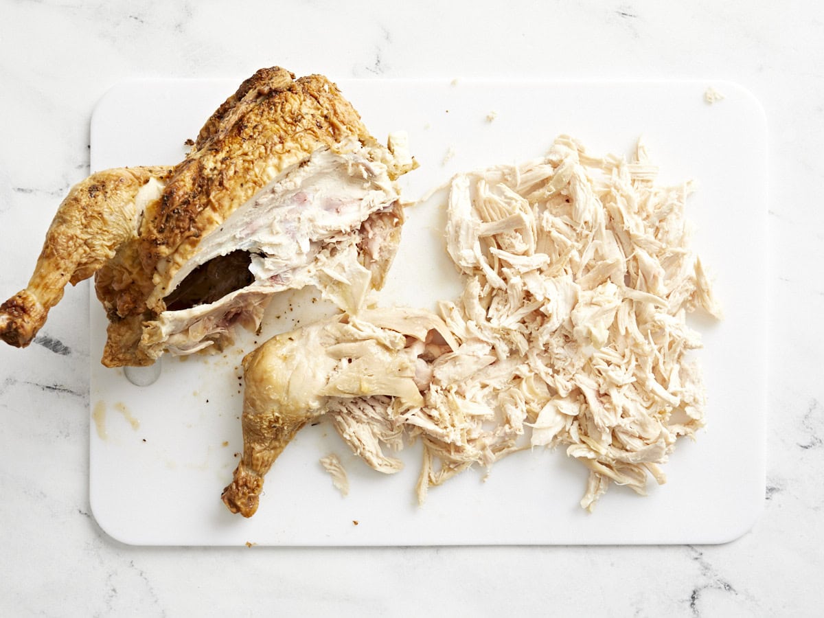 Half a rotisserie chicken and shredded chicken on a chopping board.