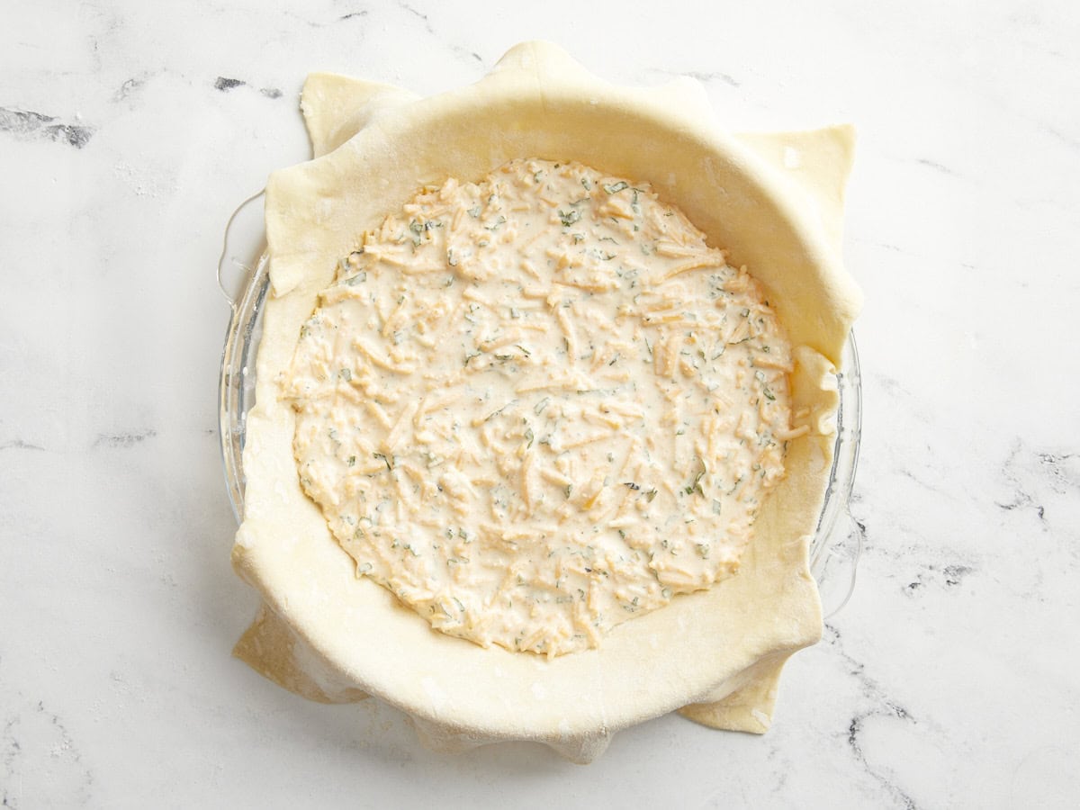 Puff pastry sheet in a glass pie pan filled with tomato pie filling