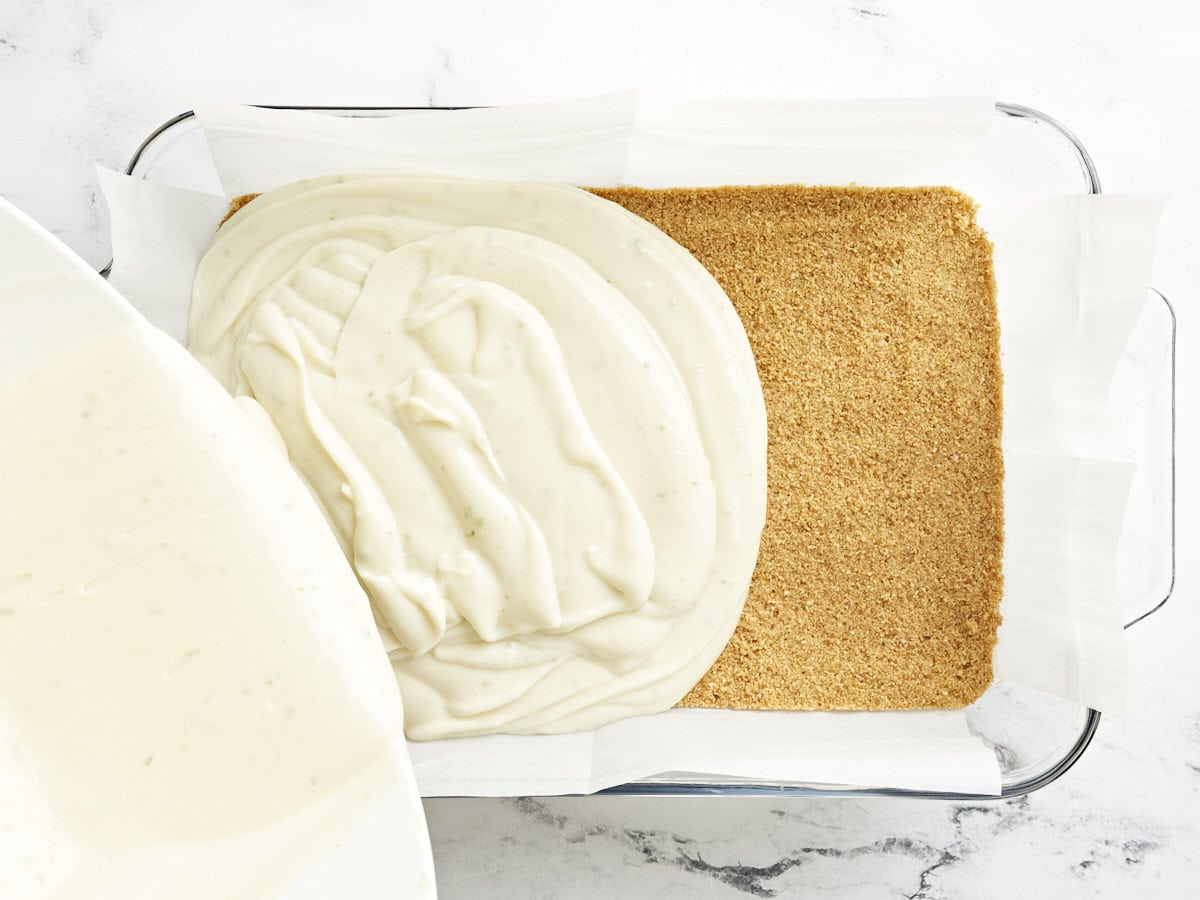 Key lime pie filling being poured over the crust in a baking dish.