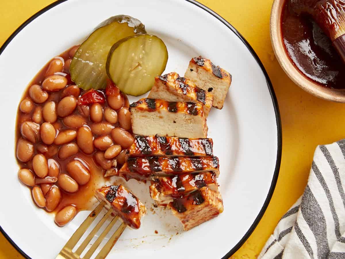 BBQ grilled tofu on a plate with baked beans and pickles.