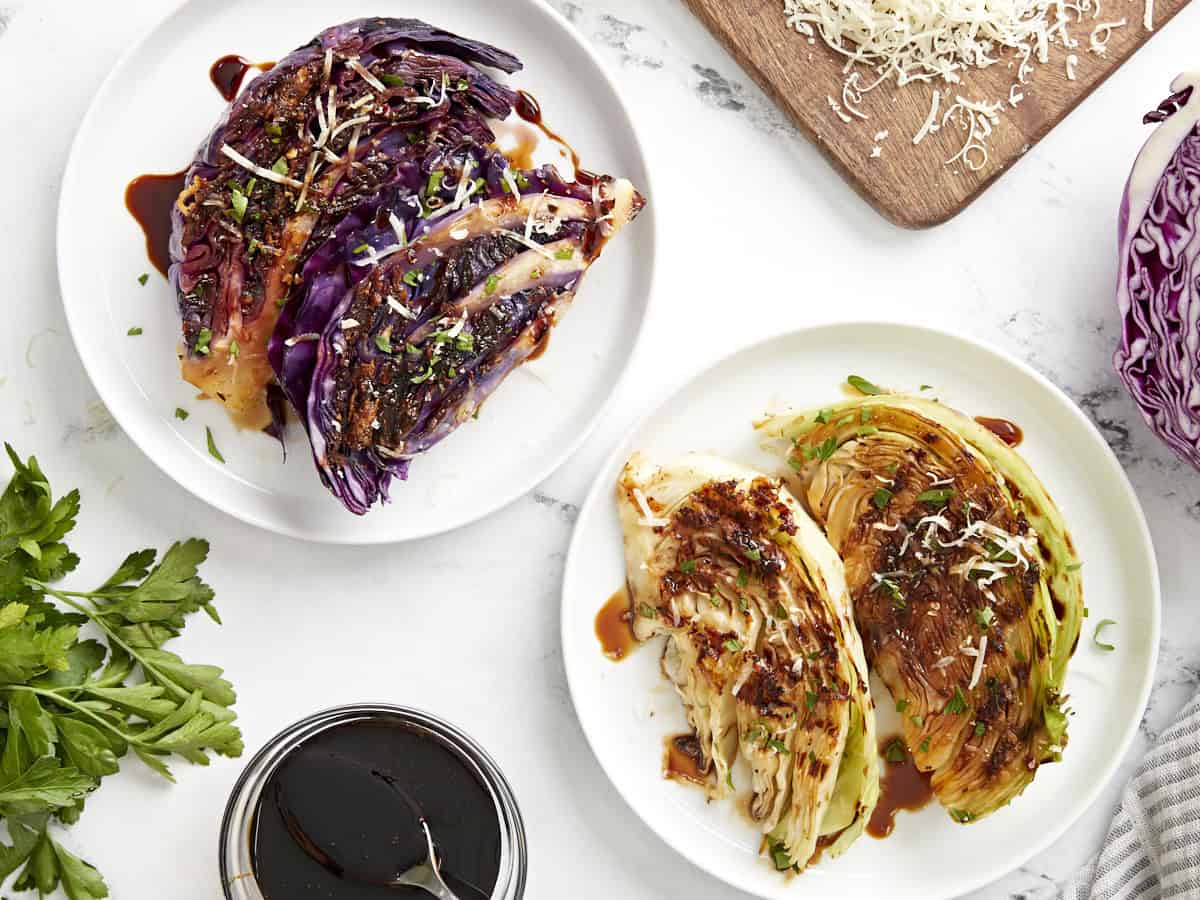 Overhead view grilled cabbage wedges on two plates, topped with balsamic glaze, Parmesan cheese, and fresh parsley.