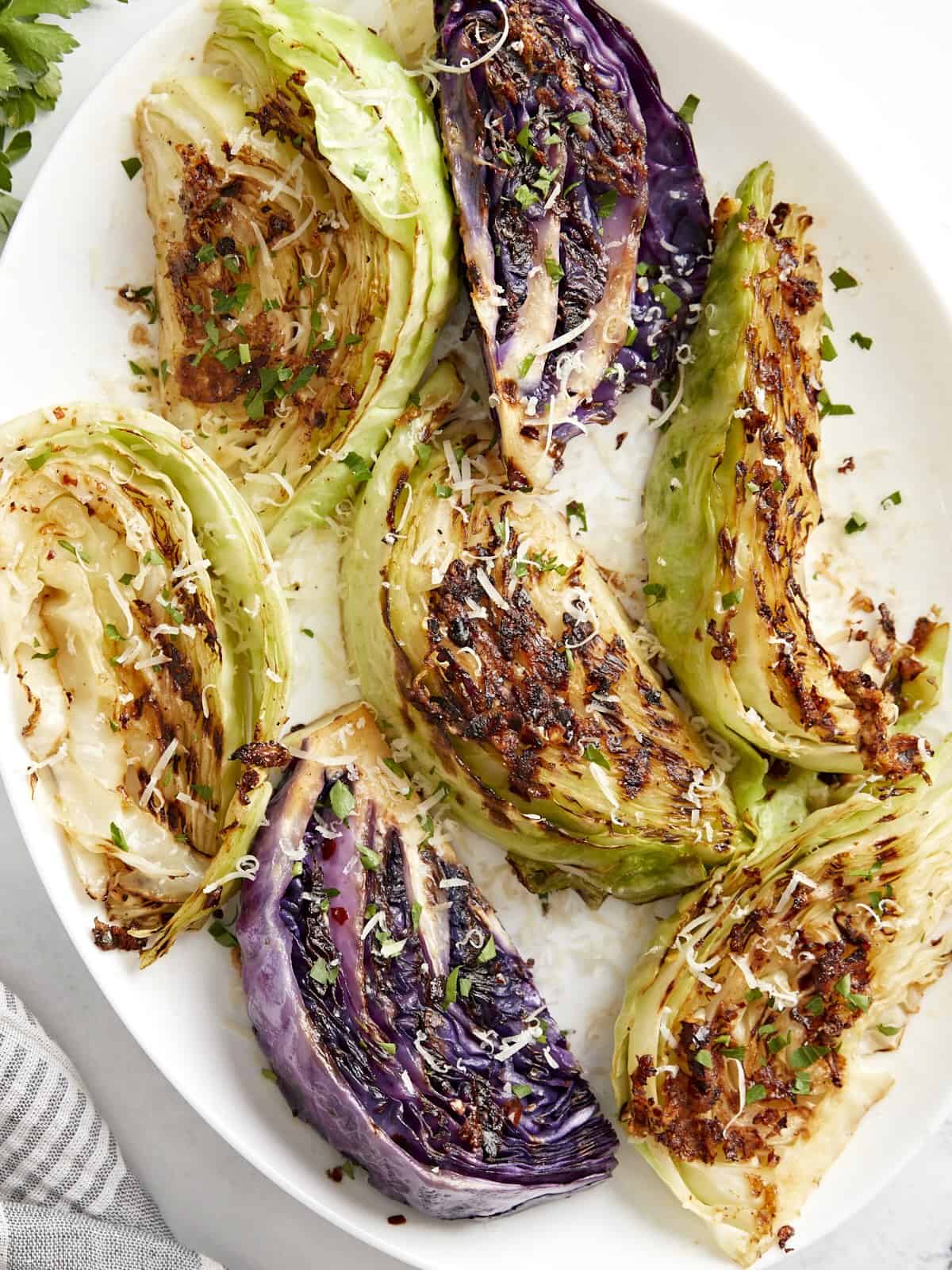 Overhead view of grilled cabbage wedges topped with balsamic glaze, Parmesan, and fresh parsley.