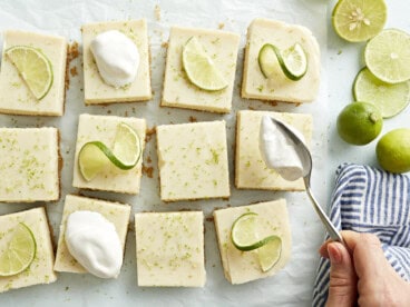 Key lime pie bars topped with whipped cream and lime slices.