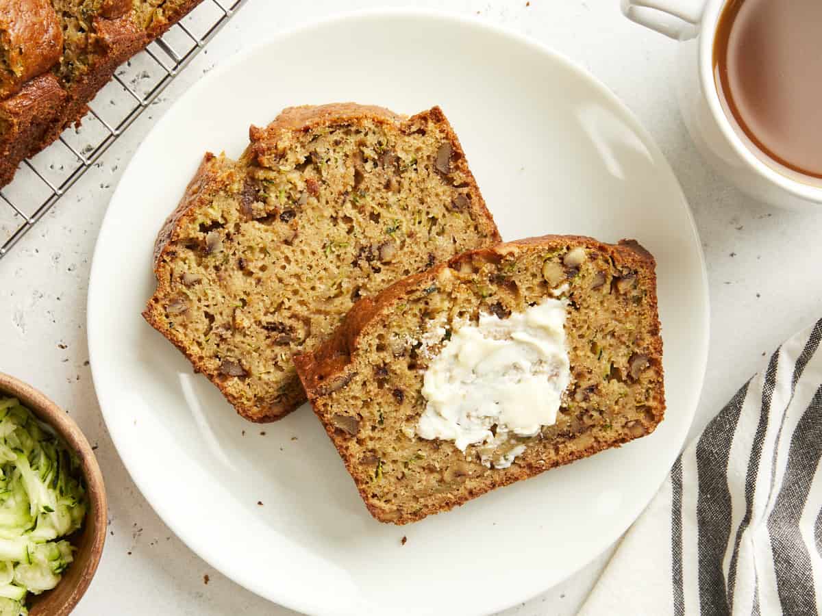 Two slices of zucchini bread on a white plate with butter spread on one slice.